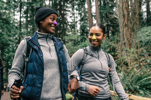 Two woman hiking while wearing Noz colorful sunscreen on their nose. 